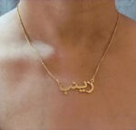 Copper necklace pendant spelling the name Zainab in Arabic calligraphy.