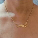 Copper necklace pendant spelling the name Zainab in Arabic calligraphy.