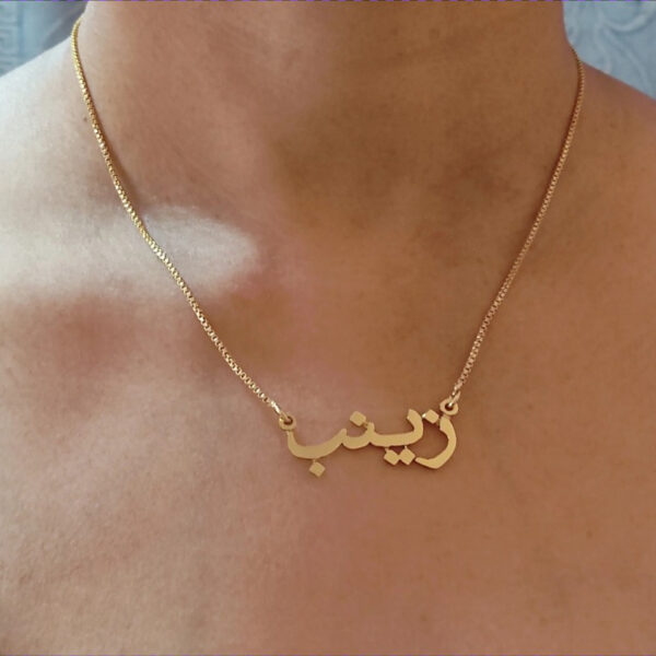 Copper necklace pendant spelling the name Zainab in Arabic calligraphy.
