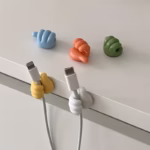 Colorful thumb-shaped cable clips holding a charging wire on a desk