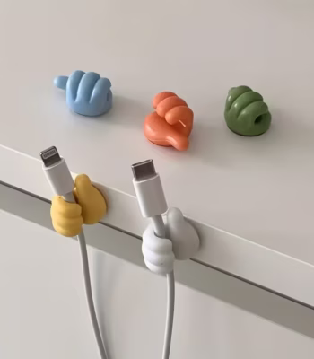 Colorful thumb-shaped cable clips holding a charging wire on a desk
