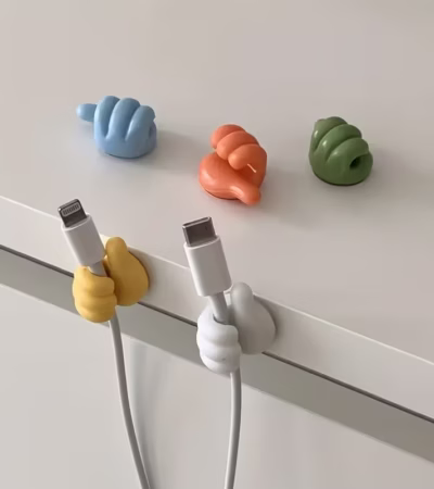 Colorful thumb-shaped cable clips holding a charging wire on a desk