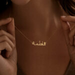 Copper necklace pendant spelling the name Fatima in Arabic calligraphy.