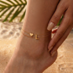 Woman wearing a letter L heart anklet with a double-layer chain and heart charm.