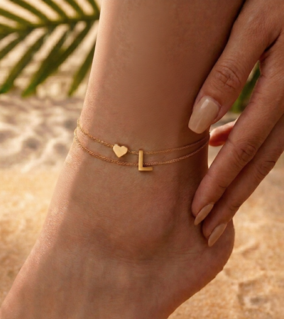 Woman wearing a letter L heart anklet with a double-layer chain and heart charm.