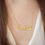 Copper necklace pendant spelling the name Fatima in Arabic calligraphy.