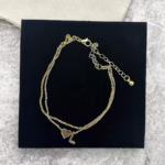 Woman wearing a letter L heart anklet with a double-layer chain and heart charm.