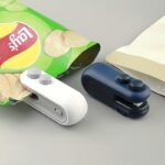 Handheld white mini bag sealer with USB-C port sealing a plastic potato chip bag.