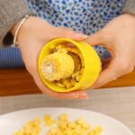 A person using the Stainless Steel Corn Stripper Peeler on a yellow corn cob.