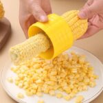 A person using the Stainless Steel Corn Stripper Peeler on a yellow corn cob.