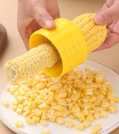 A person using the Stainless Steel Corn Stripper Peeler on a yellow corn cob.