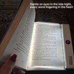 A transparent LED reading light panel placed over a paperback book page in a dark room.