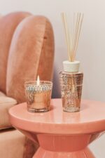 The Paris scented candle and fragrance diffuser are decorated with a powder pink and gold silk-screen print depicting the base of the Eiffel Tower's stylized structure.