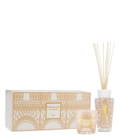 The Paris scented candle and fragrance diffuser are decorated with a powder pink and gold silk-screen print depicting the base of the Eiffel Tower's stylized structure.