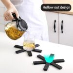 Black foldable heat insulation pot holder by Tawfeer showing the cross-shaped unfolded design on a kitchen counter.