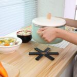 Black foldable heat insulation pot holder by Tawfeer showing the cross-shaped unfolded design on a kitchen counter.