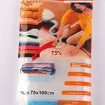 A vacuum cleaner nozzle compresses a folded blue quilt inside a transparent 70x100cm vacuum storage bag.