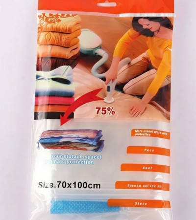 A vacuum cleaner nozzle compresses a folded blue quilt inside a transparent 70x100cm vacuum storage bag.