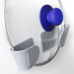 Set of three green and grey adhesive holders for saucepan lids installed on a wall.