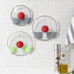 Set of three green and grey adhesive holders for saucepan lids installed on a wall.