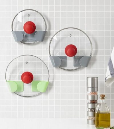 Set of three green and grey adhesive holders for saucepan lids installed on a wall.