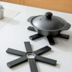 Black foldable heat insulation pot holder by Tawfeer showing the cross-shaped unfolded design on a kitchen counter.