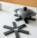 Black foldable heat insulation pot holder by Tawfeer showing the cross-shaped unfolded design on a kitchen counter.